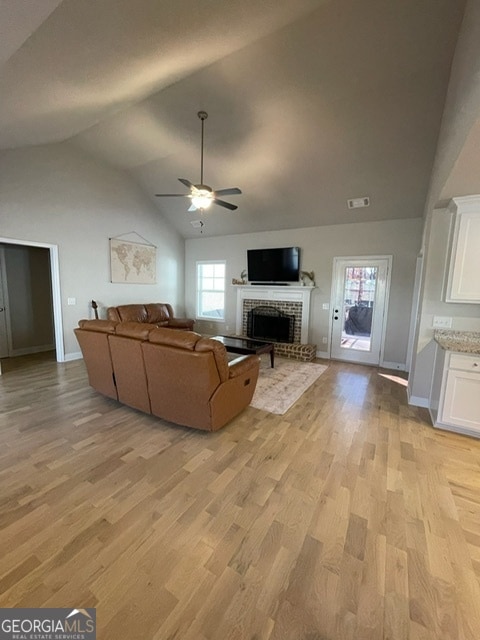 unfurnished living room featuring ceiling fan, light wood-type flooring, lofted ceiling, and a fireplace