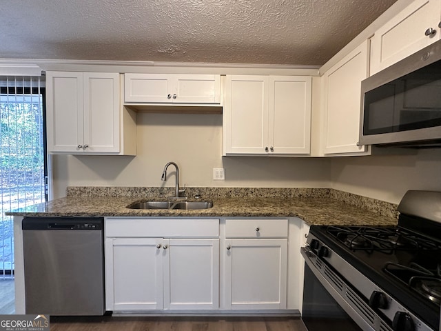 kitchen with stainless steel appliances, white cabinetry, dark stone counters, and sink