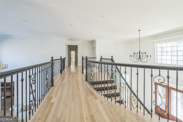 hallway featuring light wood-type flooring, crown molding, and a notable chandelier