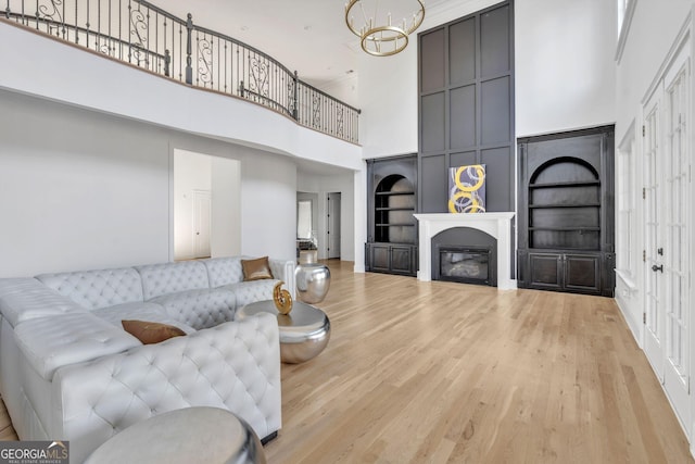 living room with built in features, a chandelier, a high ceiling, and light wood-type flooring