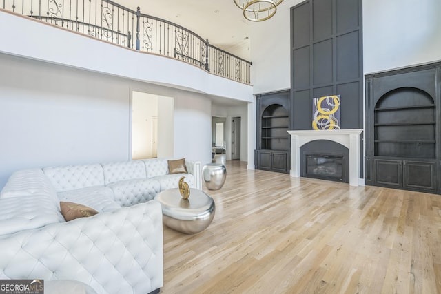 living room with built in shelves, a towering ceiling, an inviting chandelier, and light hardwood / wood-style flooring