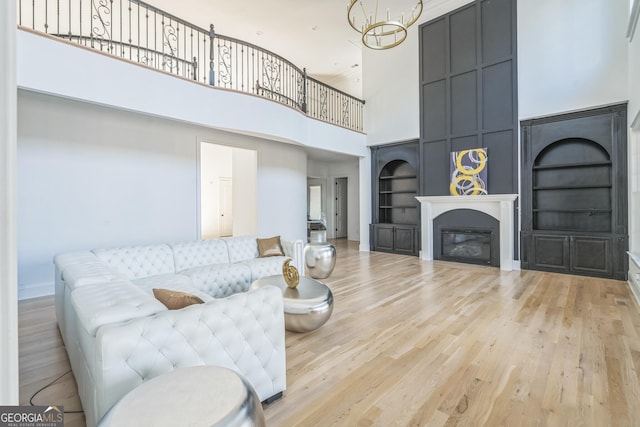 living room with a notable chandelier, built in shelves, light wood-type flooring, and a high ceiling