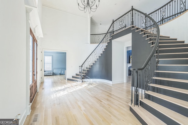 entryway featuring crown molding, light hardwood / wood-style flooring, and a towering ceiling