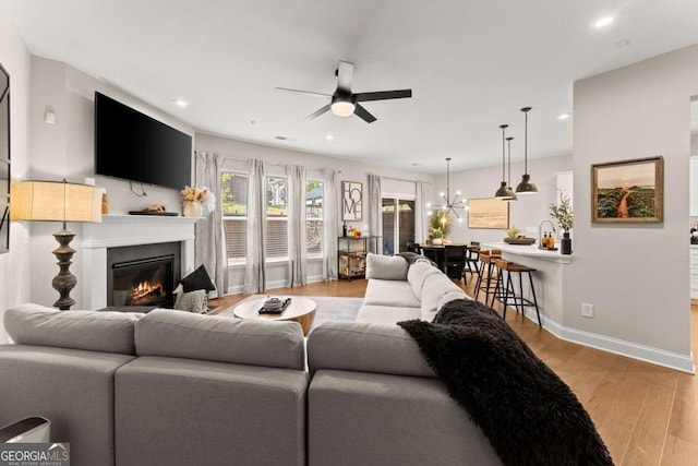 living room featuring ceiling fan with notable chandelier and light hardwood / wood-style flooring