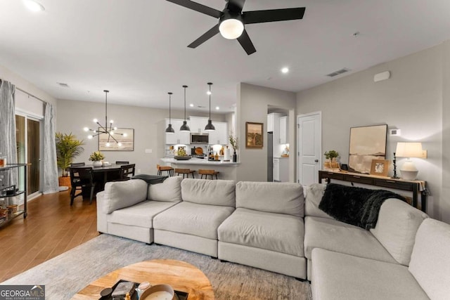 living room featuring ceiling fan with notable chandelier and light hardwood / wood-style flooring