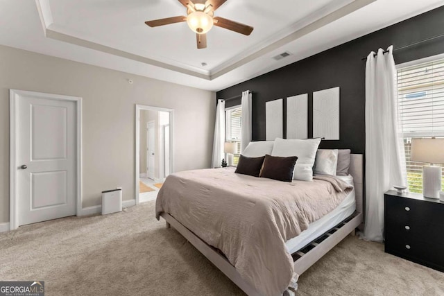 bedroom featuring ceiling fan, ensuite bathroom, a tray ceiling, and light carpet