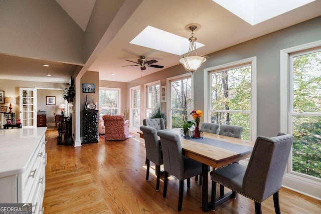 dining space featuring a skylight, ceiling fan, light hardwood / wood-style flooring, and a healthy amount of sunlight