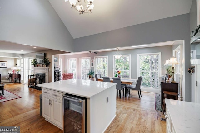 kitchen with ceiling fan with notable chandelier, high vaulted ceiling, white cabinets, light hardwood / wood-style floors, and wine cooler