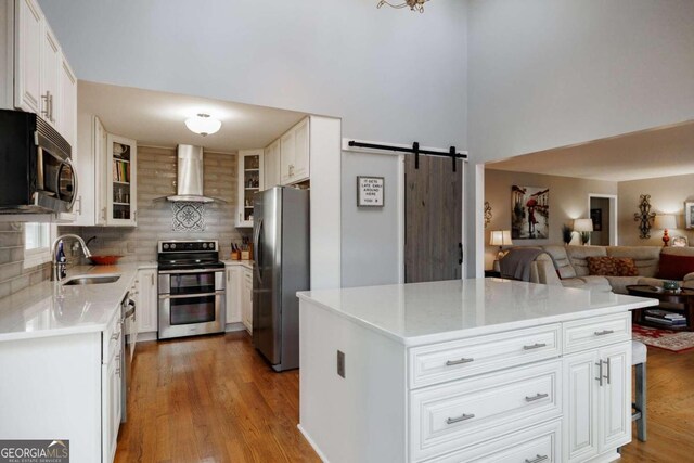 kitchen featuring white cabinets, wall chimney range hood, sink, a barn door, and appliances with stainless steel finishes