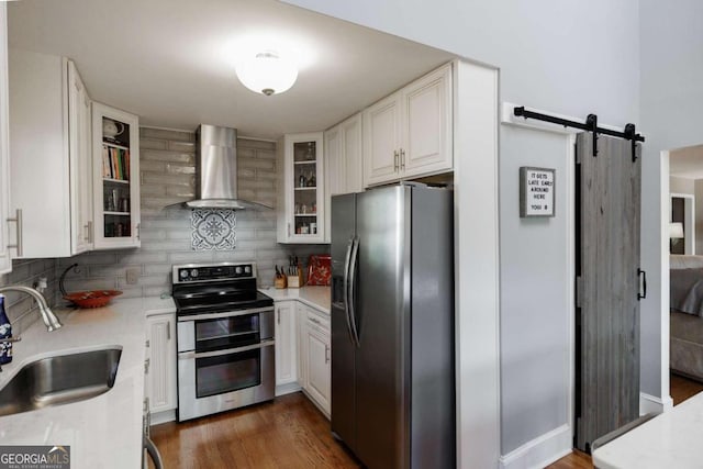 kitchen featuring white cabinetry, sink, stainless steel appliances, wall chimney range hood, and a barn door