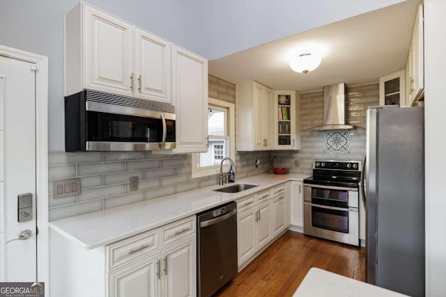 kitchen featuring backsplash, wall chimney exhaust hood, stainless steel appliances, sink, and white cabinetry