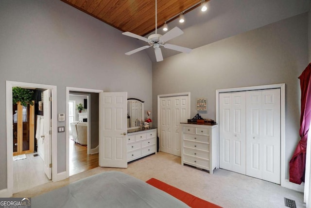 carpeted bedroom with ceiling fan, wood ceiling, high vaulted ceiling, and multiple closets