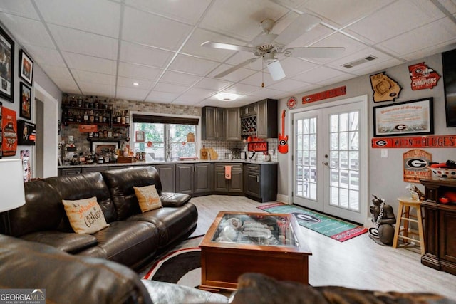 living room featuring a drop ceiling, ceiling fan, and french doors