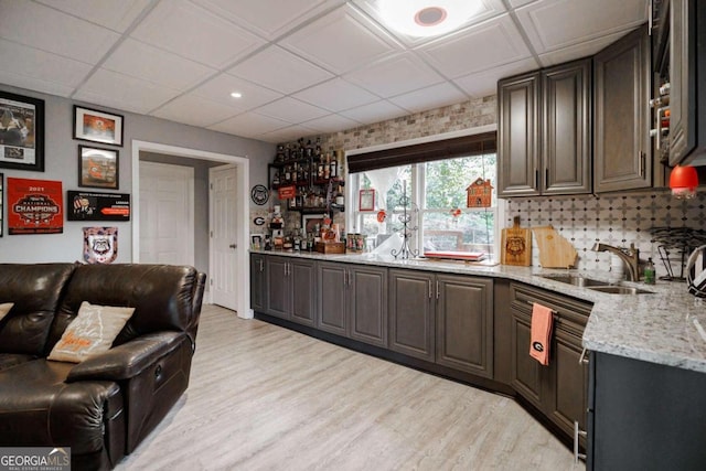 kitchen with a drop ceiling, sink, light hardwood / wood-style flooring, light stone counters, and dark brown cabinetry