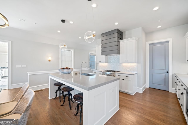 kitchen with white cabinetry, sink, an island with sink, decorative light fixtures, and hardwood / wood-style flooring