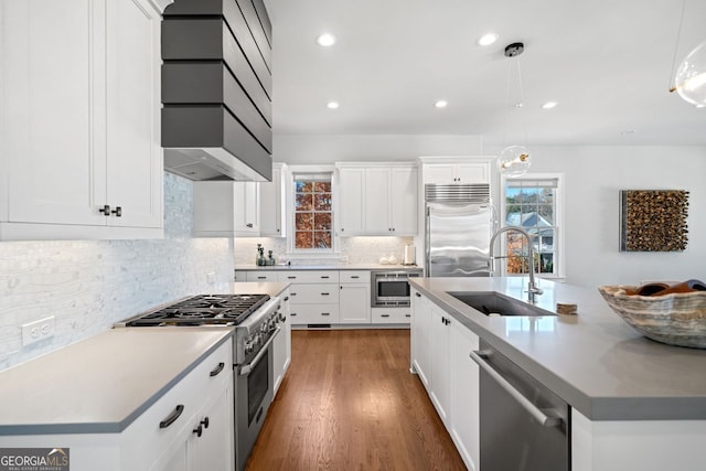 kitchen with a kitchen island with sink, dark wood-type flooring, sink, hanging light fixtures, and built in appliances