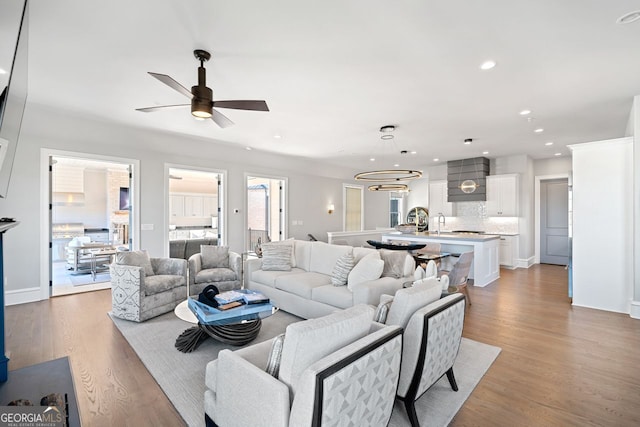 living room featuring ceiling fan with notable chandelier, light wood-type flooring, and sink