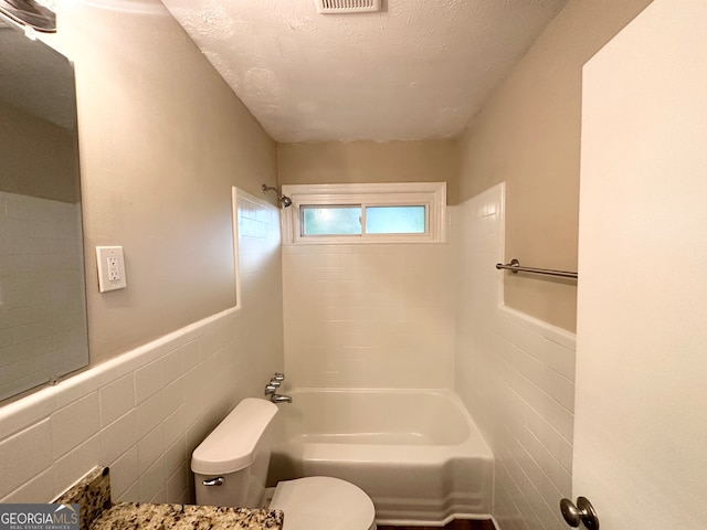 bathroom with a textured ceiling, tiled shower / bath combo, tile walls, and toilet