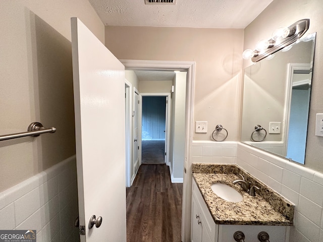 bathroom with hardwood / wood-style flooring, vanity, tile walls, and a textured ceiling