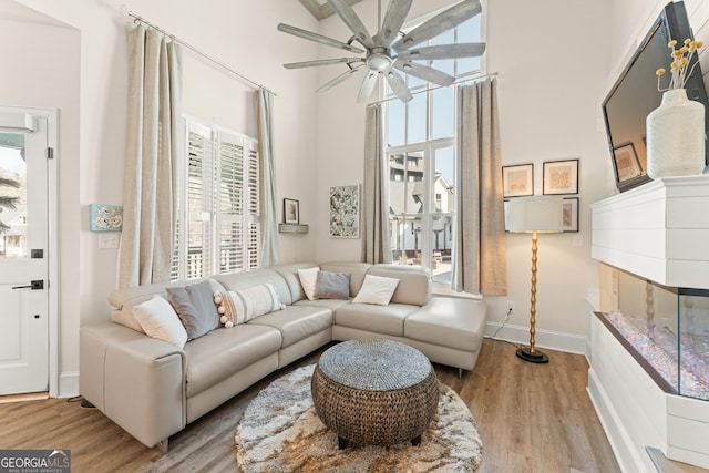 living room featuring light wood finished floors, ceiling fan, a fireplace, and baseboards