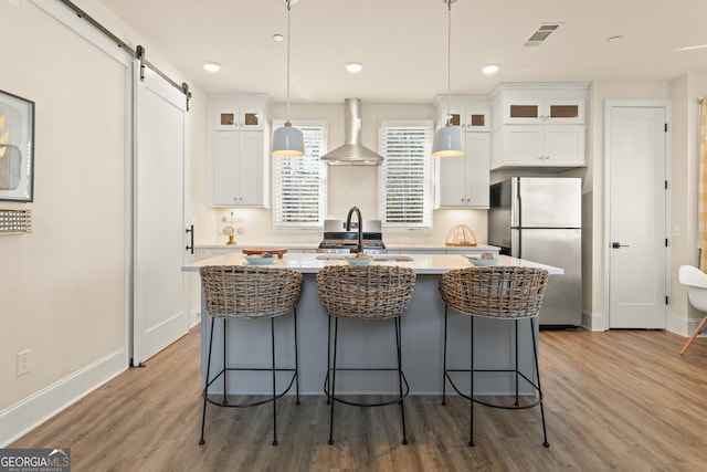 kitchen with a barn door, glass insert cabinets, freestanding refrigerator, white cabinets, and wall chimney exhaust hood