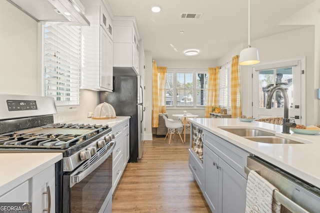 kitchen featuring stainless steel appliances, a sink, visible vents, hanging light fixtures, and light countertops