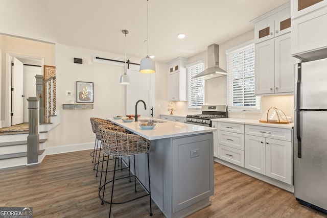 kitchen with hanging light fixtures, appliances with stainless steel finishes, glass insert cabinets, a sink, and wall chimney range hood