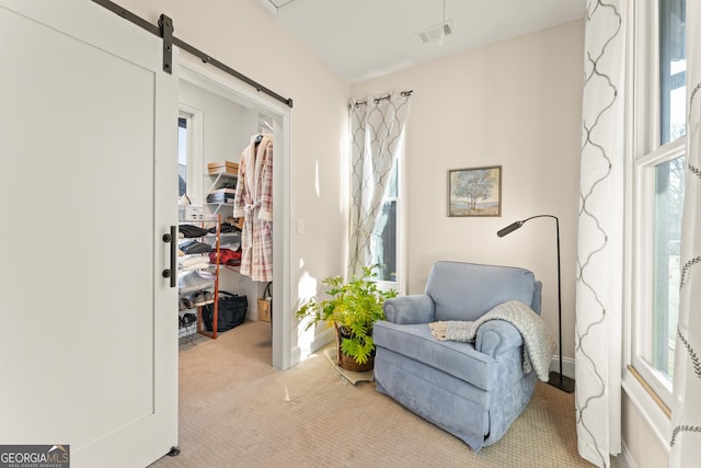 sitting room with a barn door, plenty of natural light, visible vents, and light colored carpet