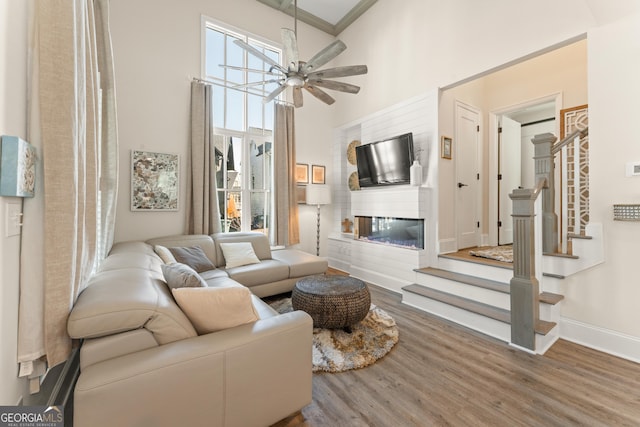 living room featuring baseboards, a glass covered fireplace, stairway, wood finished floors, and a high ceiling