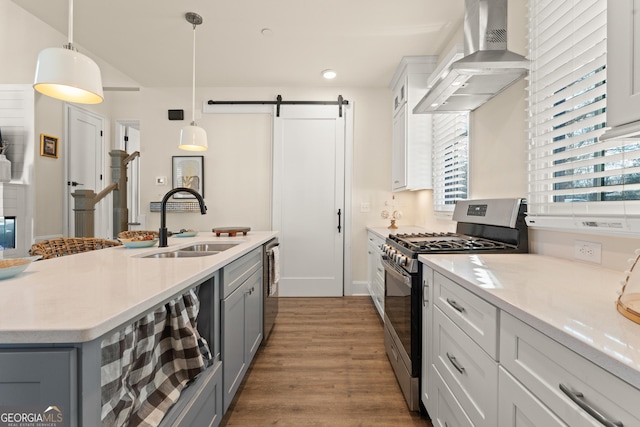 kitchen featuring a barn door, stainless steel appliances, a sink, wall chimney exhaust hood, and decorative light fixtures