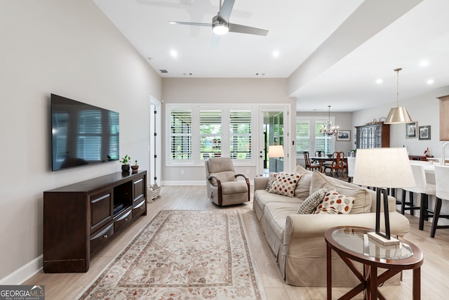 living room featuring ceiling fan with notable chandelier and light hardwood / wood-style flooring