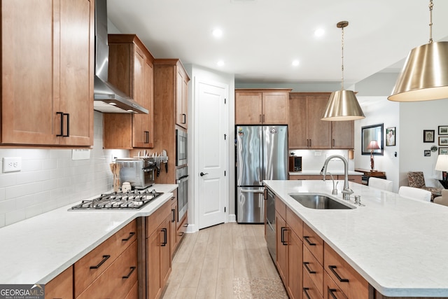 kitchen with wall chimney range hood, sink, hanging light fixtures, light hardwood / wood-style flooring, and stainless steel appliances