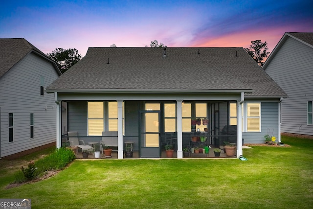 back house at dusk featuring a sunroom and a lawn