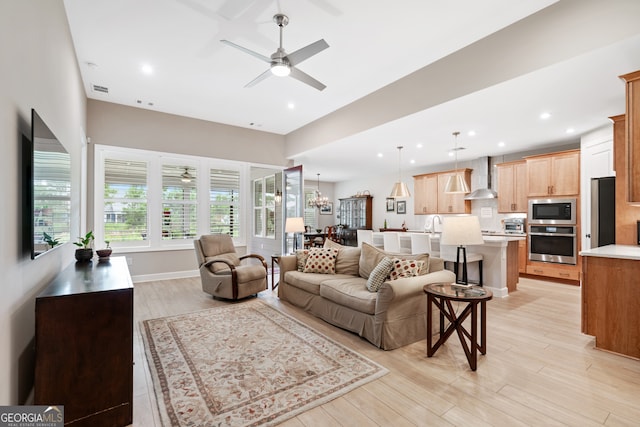 living room featuring ceiling fan with notable chandelier and light wood-type flooring