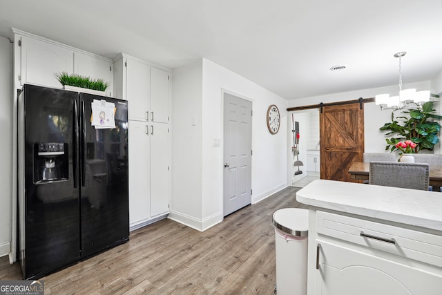 kitchen featuring white cabinetry, a barn door, black refrigerator with ice dispenser, light hardwood / wood-style flooring, and pendant lighting