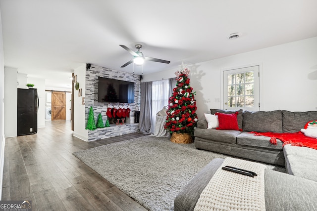 living room with a barn door, ceiling fan, dark hardwood / wood-style flooring, and washer / dryer