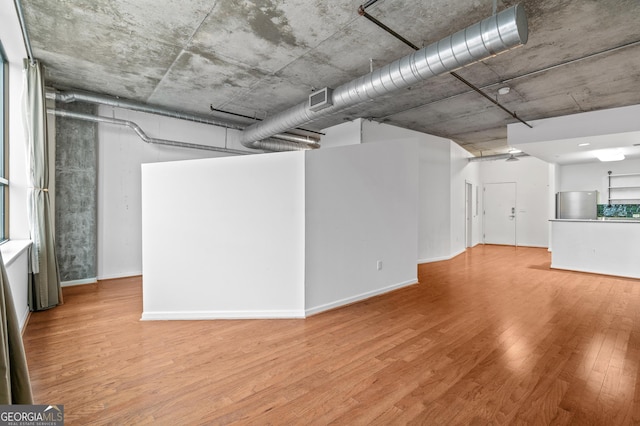 basement featuring light wood finished floors, baseboards, visible vents, and freestanding refrigerator