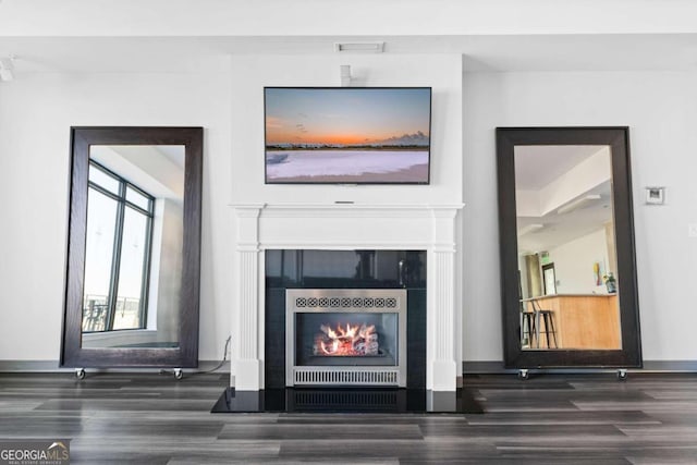 interior space with a tile fireplace, wood finished floors, visible vents, and baseboards