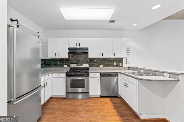 kitchen featuring a peninsula, stainless steel appliances, light countertops, under cabinet range hood, and a sink