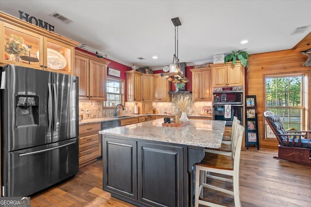 kitchen featuring stainless steel refrigerator with ice dispenser, a center island, plenty of natural light, and double oven