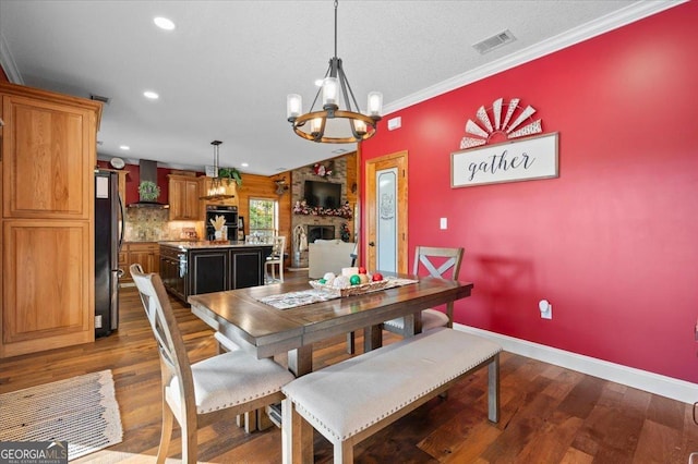 dining area with a large fireplace, hardwood / wood-style flooring, an inviting chandelier, and ornamental molding