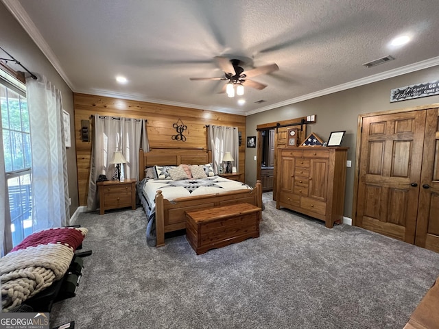 carpeted bedroom featuring wood walls, ceiling fan, a barn door, ornamental molding, and a textured ceiling