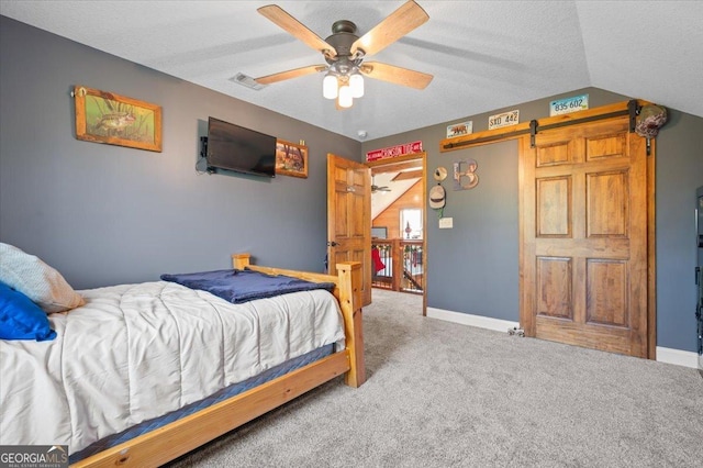 carpeted bedroom with a textured ceiling, a barn door, vaulted ceiling, and ceiling fan