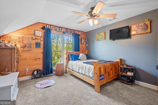 carpeted bedroom with a textured ceiling, vaulted ceiling, ceiling fan, and wooden walls