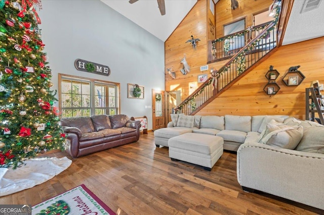 living room with ceiling fan, wood walls, dark wood-type flooring, and high vaulted ceiling