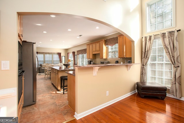 kitchen with a kitchen breakfast bar, stainless steel fridge, light wood-type flooring, black oven, and kitchen peninsula