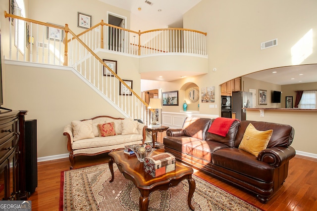 living room featuring a towering ceiling, a healthy amount of sunlight, and hardwood / wood-style flooring