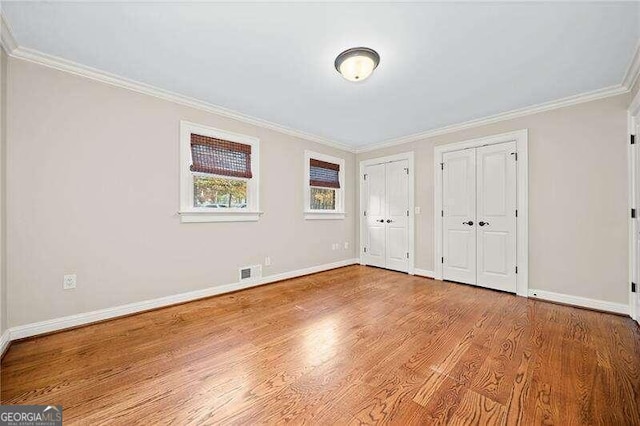 unfurnished bedroom featuring two closets, light hardwood / wood-style flooring, and ornamental molding