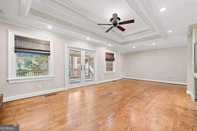 unfurnished living room with plenty of natural light, light wood-type flooring, crown molding, and a tray ceiling