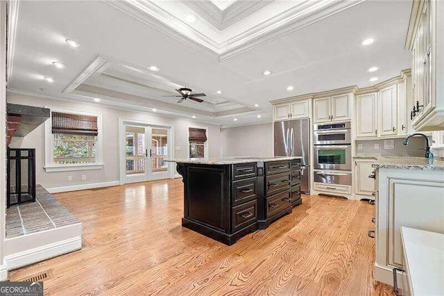 kitchen with a center island, a raised ceiling, crown molding, light wood-type flooring, and appliances with stainless steel finishes